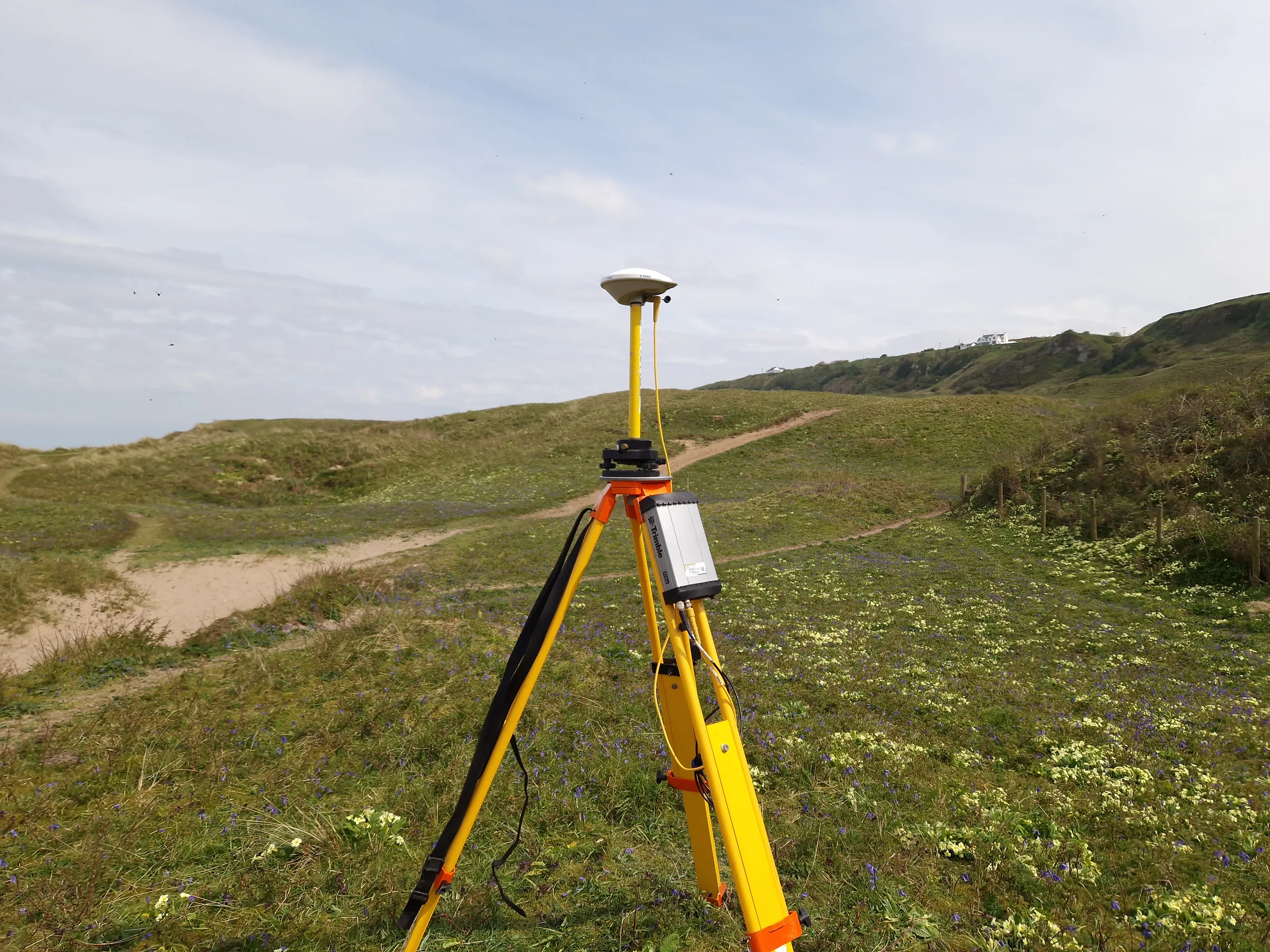 A GNSS reference station antenna mounted on a survey tripod on grassy coastal dunes
